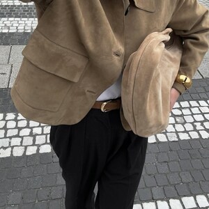 Woman wearing beige minimalist leather jacket with oversized suede bag and neutral outfit