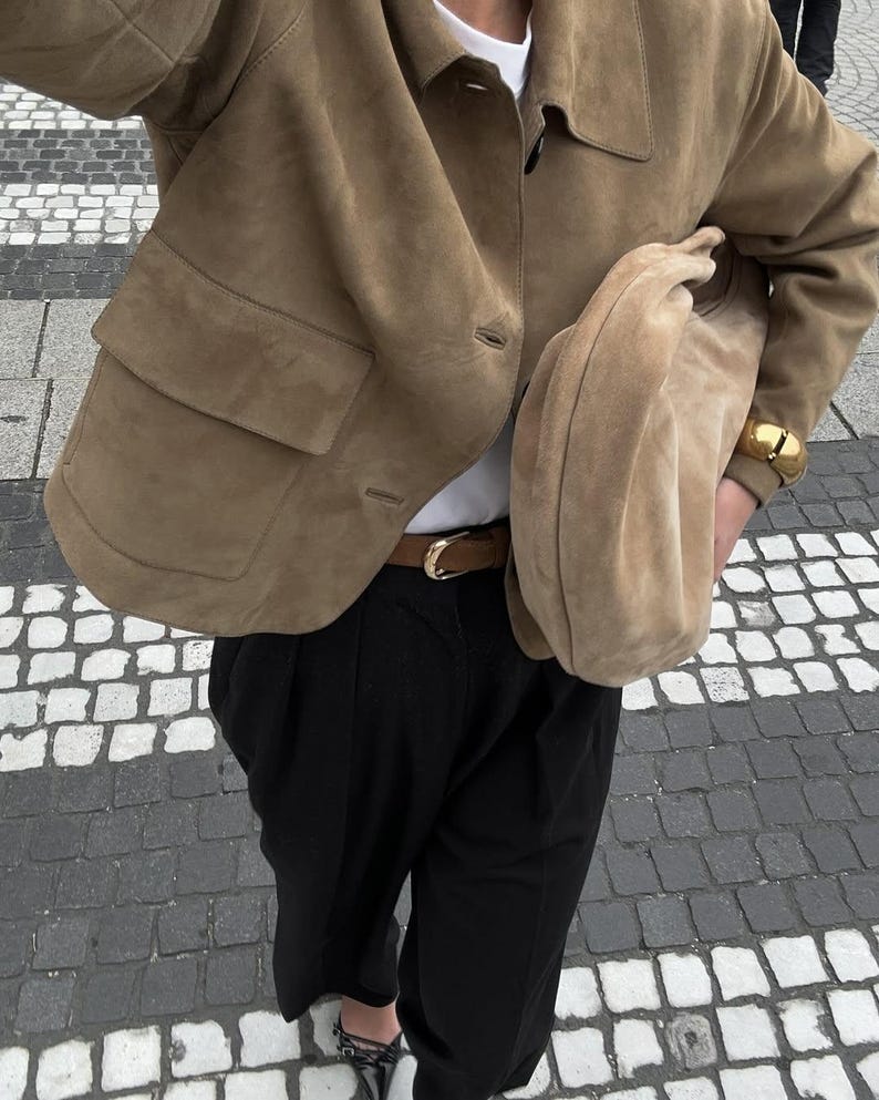 Woman wearing beige minimalist leather jacket with oversized suede bag and neutral outfit
