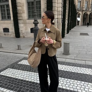 Woman standing in beige leather jacket with relaxed fit and parisian style outfit outdoors