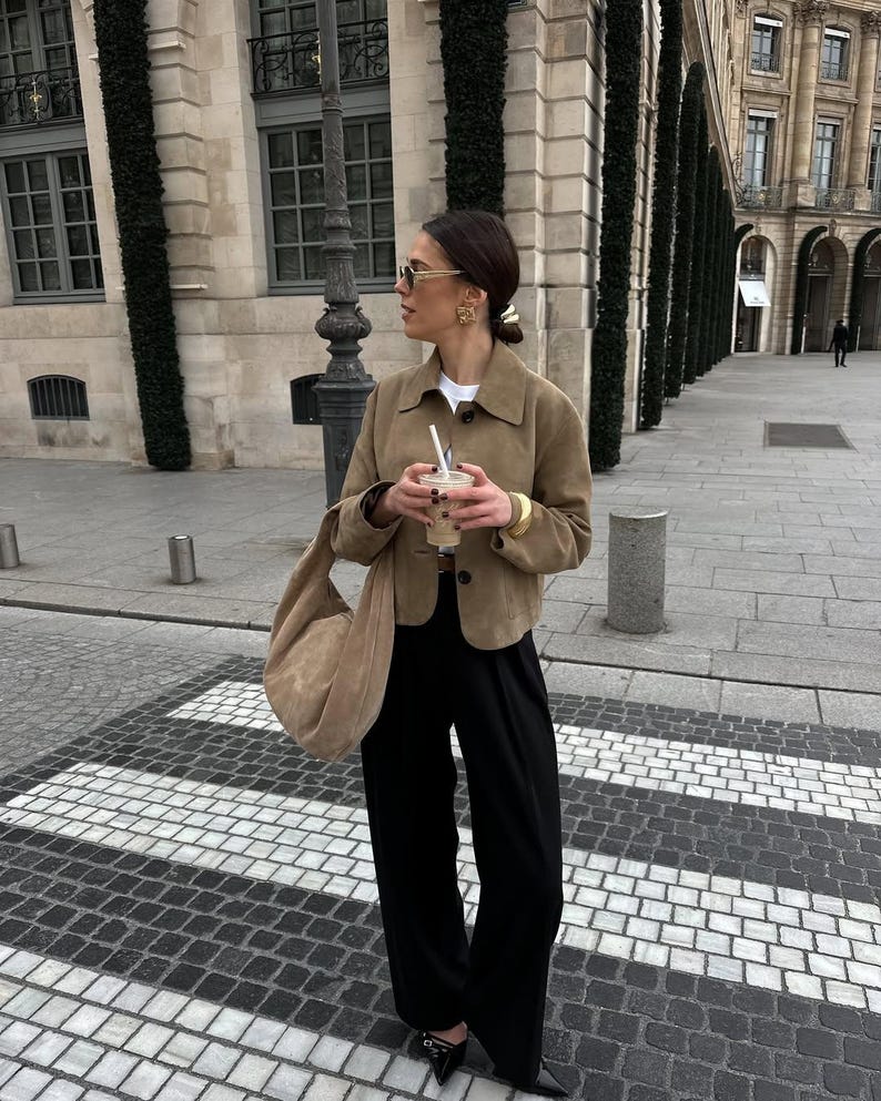 Woman standing in beige leather jacket with relaxed fit and parisian style outfit outdoors