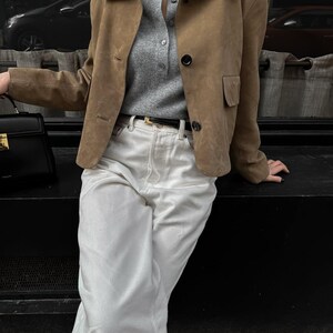 Model sitting in beige leather jacket with white pants and minimalist chic everyday outfit