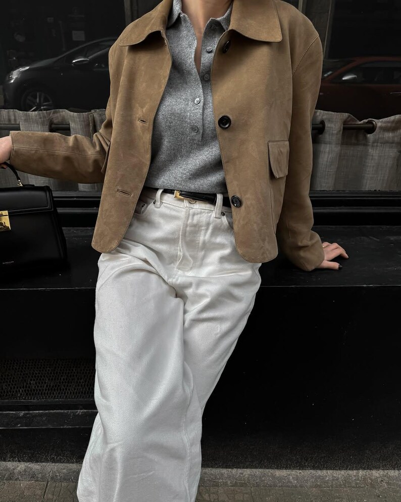 Model sitting in beige leather jacket with white pants and minimalist chic everyday outfit