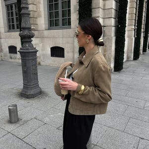 Woman walking in beige leather jacket with black trousers and quiet luxury outfit street style