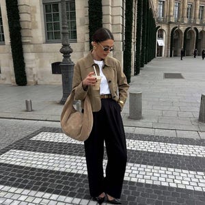 Woman holding coffee wearing beige leather jacket with black pants and quiet luxury style