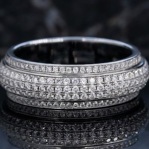 May include: A silver-toned metal ring featuring a wide, rounded band completely encrusted with multiple rows of small, clear, sparkling stones. The design includes a central section with three rows of stones flanked by two thinner rows on each side.