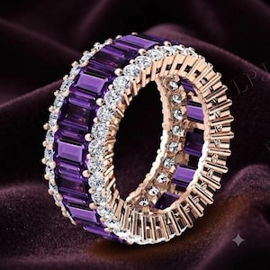 Op de afbeelding: Een eeuwigheidsring van roségoud met een centrale rij rechthoekige, baguette-geslepen paarse amethisten, geflankeerd door twee rijen kleine, ronde, helderwitte diamanten. De ring is volledig bezet met deze edelstenen in een doorlopend patroon.