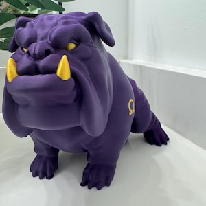 Könnte beinhalten: Eine lila Bulldoggenfigur mit gelben Augen und Zähnen. Der Bulldogge hat einen muskulösen Körperbau und einen ernsten Gesichtsausdruck. Auf der Seite der Bulldogge befindet sich ein goldfarbener griechischer Buchstabe.