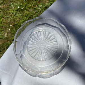 Peut inclure: Une assiette en verre transparent dotée d'un bord festonné et d'un motif central en rayons de soleil avec des lignes rayonnantes. L'assiette présente une surface lisse et transparente ainsi qu'une forme circulaire, avec un design en verre pressé.