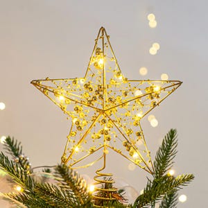 Könnte beinhalten: Ein goldfarbener Stern für die Spitze des Weihnachtsbaums mit einem Drahtrahmen-Design. Der Stern ist mit kleinen, runden, goldfarbenen Perlen verziert und mit warmweißen Lichtern beleuchtet. Er ist auf einer goldfarbenen Spiralbasis montiert.