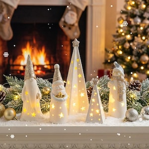 以下が含まれることがあります： クリスマスの装飾品。光るセラミック製の置物で、ノーム、サンタクロース、星型のツリーが含まれています。すべて金色のアクセントと星の切り抜きが施されています。暖炉と装飾されたクリスマスツリーを背景に配置されています。