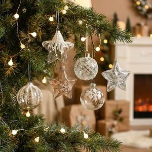 Peut inclure: Gros plan sur un sapin de Noël orné de décorations en verre transparent. Les décorations comprennent des formes d'étoiles et de boules, certaines avec des paillettes et des motifs de flocons de neige. Des guirlandes lumineuses blanches chaudes sont accrochées dans l'arbre.