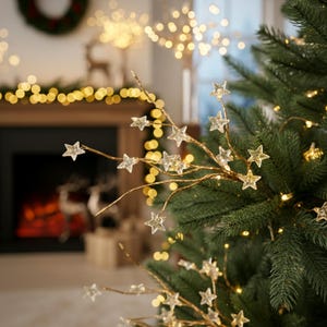 以下が含まれることがあります： 金色のワイヤーの枝に星型のライトが付いたクリスマスツリーのクローズアップ。木は緑の針と小さな温白色のライトで飾られています。背景には暖炉やその他のクリスマスの装飾が写っています。