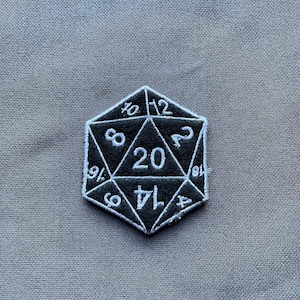 May include: Embroidered D20 die patch in black and white. The twenty-sided die has white numbers on a black background. The numbers are stitched in a clear, easy-to-read font. A fun accessory for gamers, this patch is ideal for clothing or bags.