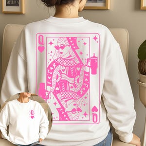May include: White sweatshirt featuring a pink Queen of Hearts playing card design on the back. The graphic includes a woman wearing sunglasses and holding a tumbler. A smaller version of the design is on the front.