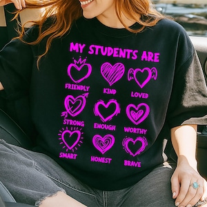May include: Black sweatshirt with the text "MY STUDENTS ARE" in bright pink. Below the text are nine pink hearts, each with a different word: Friendly, Kind, Loved, Strong, Enough, Worthy, Smart, Honest, and Brave.