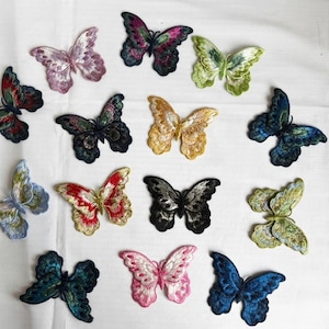May include: A collection of fourteen embroidered butterfly patches in various colours including pink, purple, yellow, red, blue, green, black, and white. Each patch features intricate thread detailing and distinct wing patterns arranged in a group.