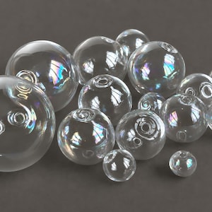 May include: A collection of clear glass spheres of varying sizes, each featuring a small circular opening and an iridescent finish that reflects light with subtle rainbow hues. The spheres are arranged in a cluster, showcasing their smooth, rounded surfaces and transparent quality.