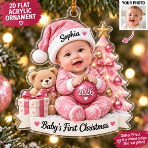 May include: A 2D flat acrylic Christmas ornament featuring a baby wearing a pink snowflake-patterned outfit and a matching Santa hat with the name Sophia. The baby holds a glittery pink ornament labeled 2026 next to a teddy bear and gift.