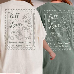 May include: An off-white and a sage green t-shirt, each featuring a back graphic of a postage stamp design with pumpkins, flowers, and the text: fall in Love, est. 2026, Emily's Bachelorette, and AUSTIN, TX, with wavy postmark lines.