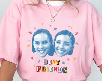 May include: Pink t-shirt with a white collar featuring two smiling faces and the words "BEST FRIENDS" in colorful letters. The design includes star accents. The shirt is a casual style.
