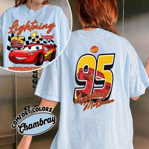 Może przedstawiać: Jasnoniebieska koszulka z Lightning McQueen z filmu Auta. Grafika z przodu zawiera Lightning McQueen, numer 95 i napis "Lightning". Tył koszulki ma dużą grafikę "95" z Lightning McQueen i napisem "Lightning McQueen".