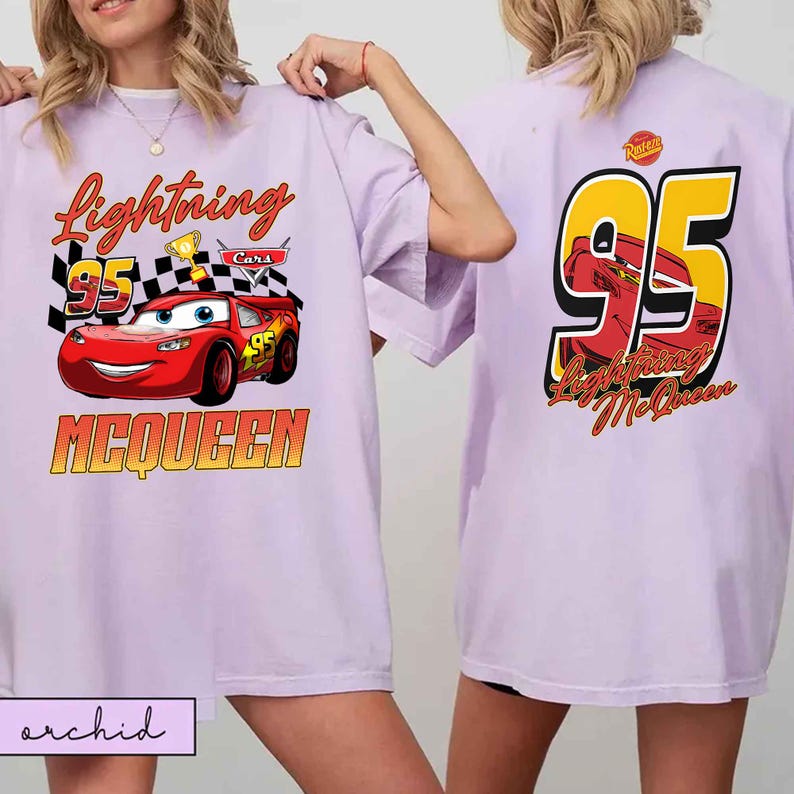 Może przedstawiać: Jasnofioletowa koszulka z Lightning McQueen z filmu Auta. Prz&oacute;d przedstawia napis "Lightning 95 McQueen" z motywem samochodu wyścigowego. Tył koszulki pokazuje duży "95" z wizerunkiem McQueena.