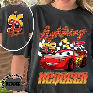 Może przedstawiać: Ciemnoszara koszulka z Lightning McQueen z filmu Auta. Grafika z przodu zawiera numer 95, szachownicę oraz słowa "Lightning" i "McQueen". Tył koszulki r&oacute;wnież przedstawia numer 95 i imię "Lightning McQueen".