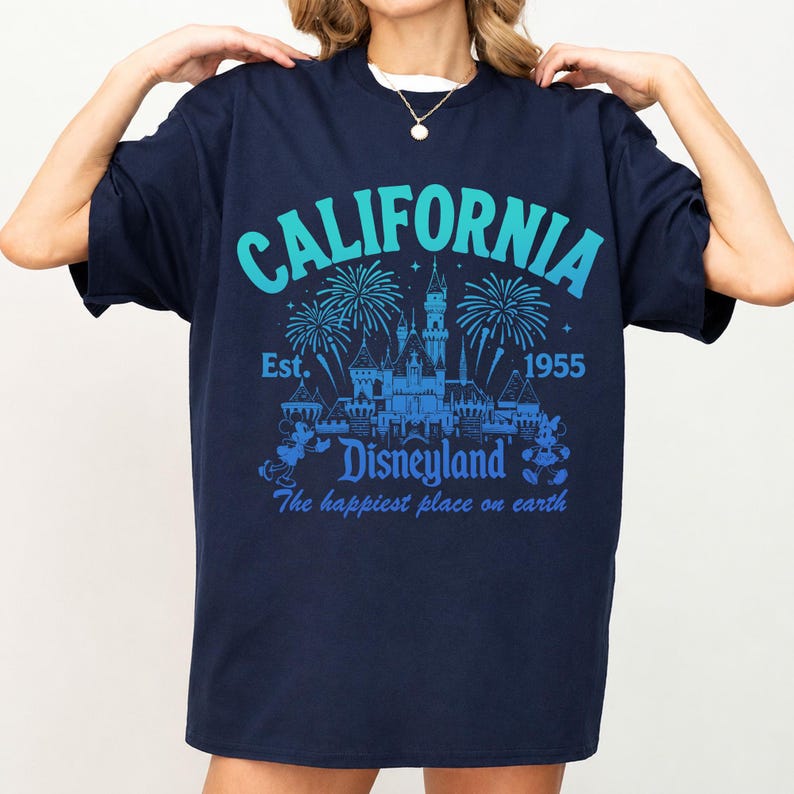 May include: Navy blue t-shirt with a teal and blue graphic. The graphic includes the word "CALIFORNIA" above a castle illustration, fireworks, and the text "Disneyland" and "The happiest place on earth."