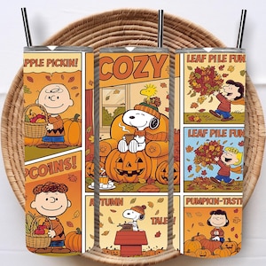 May include: A stainless steel tumbler featuring a comic strip design with fall themes. The tumbler has images of Snoopy, Charlie Brown, pumpkins, and autumn leaves. Text includes "Apple Pickin!", "Cozy", "Leaf Pile Fun", and "Pumpkin-Tasti".