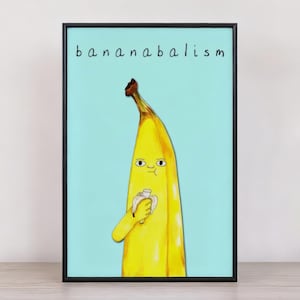 May include: A framed art print featuring a cartoon banana character with a face, holding a napkin. The banana is yellow with a brown tip, set against a light blue background. The word "bananabalism" is written above the banana.