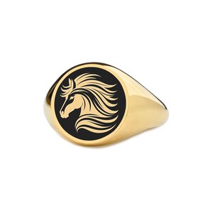 Op de afbeelding: Een gouden zegelring met een zwart cirkelvormig embleem met een paardenkop in profiel. Het paard heeft een vloeiende manen en de ring heeft een gepolijst, reflecterend oppervlak. De ring staat tegen een witte achtergrond.