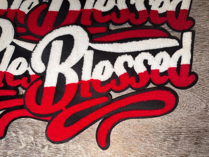 Puede incluir: Primer plano de varios parches bordados con la palabra "Blessed" en una fuente de escritura. Los parches presentan un fondo negro con letras blancas, rojas y negras. Los parches son probablemente para ropa o accesorios.