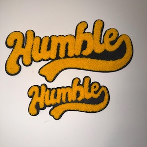 May include: Two yellow and black felt patches with the word "Humble" in a script font. The patches are in two sizes, with the larger one on top. The word is in yellow with a black outline.