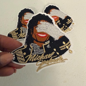 May include: Three embroidered patches featuring a stylized portrait of Michael Jackson. The design shows a figure with dark hair, a red smile, and a silver sequined glove covering the eyes. The jacket is black with gold accents and the name Michael Jackson.