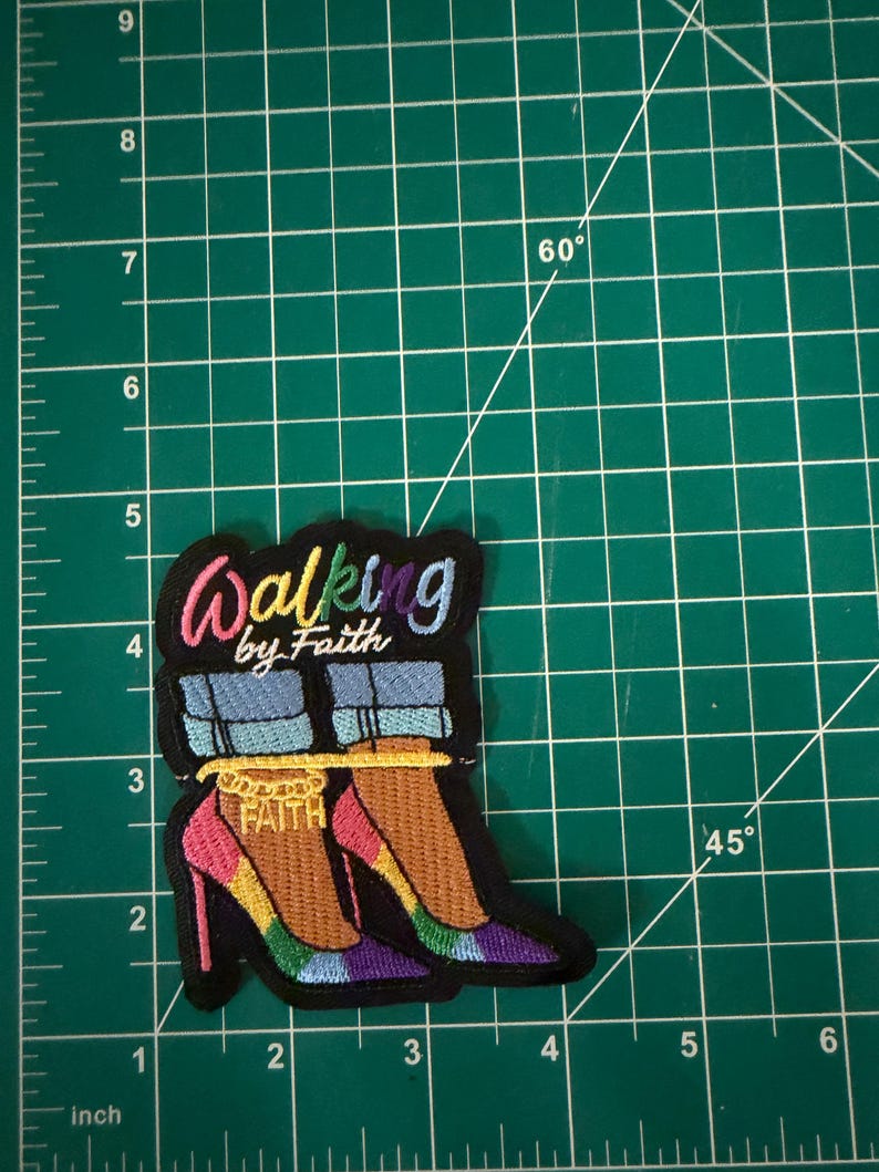 May include: An embroidered patch featuring the text Walking by Faith in colorful lettering above an illustration of two feet wearing blue jeans and high-heeled shoes with a gold anklet that reads FAITH, measuring approximately 3.5 inches tall.