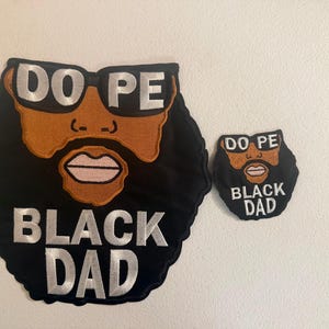 May include: Two embroidered patches with a cartoon face design. The larger patch features a black beard, brown skin, and sunglasses with the text "DO PE" and "BLACK DAD" in silver. The smaller patch has the same design.