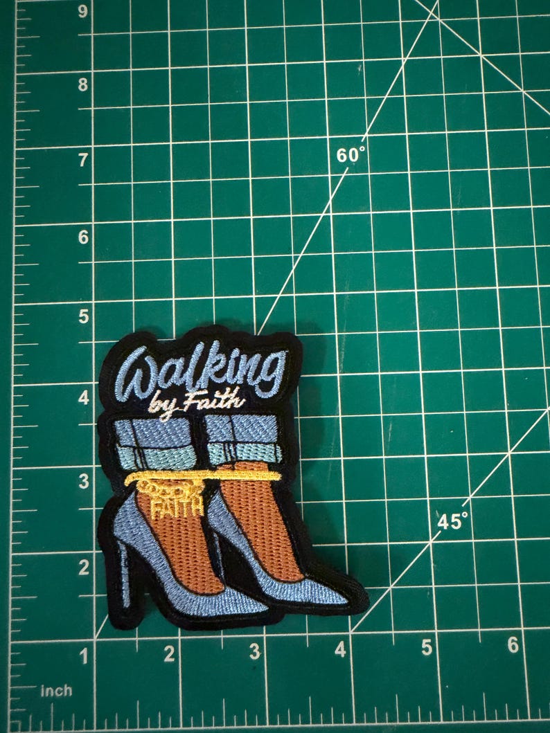 May include: An embroidered patch featuring light blue high-heeled shoes with cuffed denim jeans, a gold chain anklet with the word FAITH, and the text Walking by Faith in light blue script, measuring approximately 3.5 inches in height.