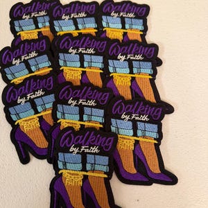 May include: A collection of embroidered patches featuring a pair of purple high-heeled shoes with light blue cuffed jeans and a gold ankle chain that reads FAITH. The text WALKING by Faith is embroidered in purple and white above the shoes.