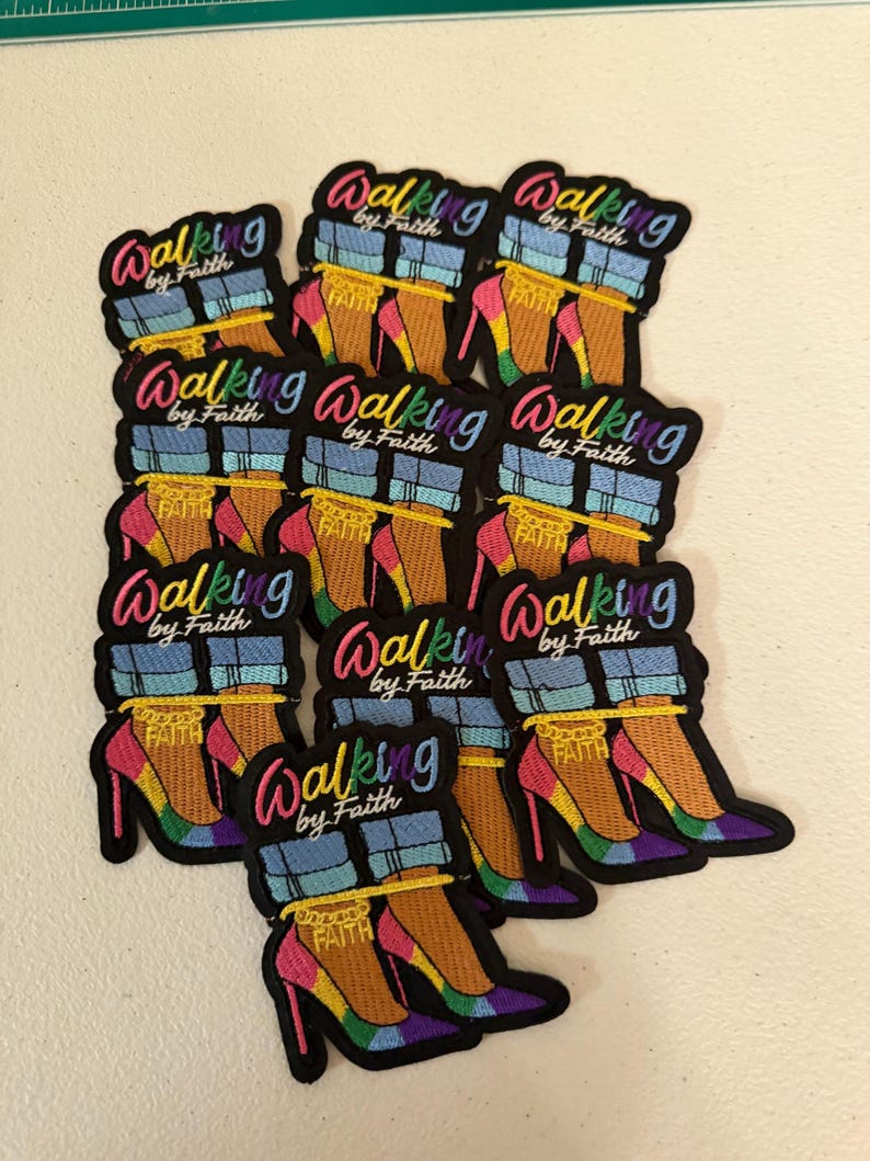 May include: A collection of embroidered patches featuring a pair of high-heeled shoes with rainbow-colored soles, blue denim cuffs, and a gold chain anklet with the word FAITH. The text Walking by Faith is embroidered in a colorful script above the shoes.