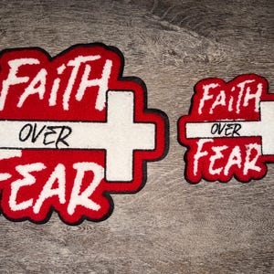 May include: Two red and white patches with the words "FAITH OVER FEAR" in a bold, stylized font. The patches feature a white cross design and a black border. One patch is larger than the other.