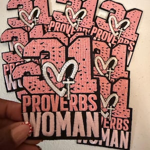 May include: Pink and black embroidered patches with the number 31, a heart, and a cross design. The patches also feature the words "PROVERBS WOMAN" and "PROVERBS MAN" in white and pink thread. The patches are stacked.