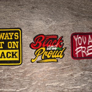 May include: Three embroidered patches with text. One is yellow with black text reading "ALWAYS BET ON BLACK." The second is red, black, yellow, and green with "Black and Proud." The third is red with white text, "YOU ARE FREE."
