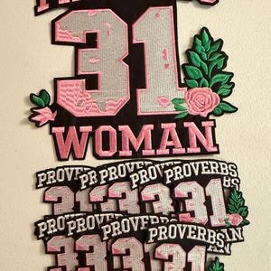 May include: A collection of embroidered patches featuring the text PROVERBS 31 WOMAN in pink and black. The design includes a large silver number 31, green leaves, and a pink rose. The patches are arranged in a stack with one large patch on top.