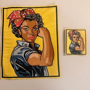 May include: Two embroidered patches featuring a woman flexing her bicep, a symbol of strength. The woman has dark skin, curly hair, and a red and white polka-dot bandana. The patches are on a yellow background with a black border.