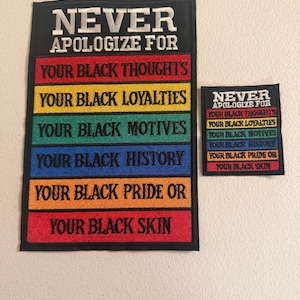 May include: Two black rectangular patches with white embroidered text. The larger patch reads "NEVER APOLOGIZE FOR" above a series of colored lines with text: "YOUR BLACK THOUGHTS", "YOUR BLACK LOYALTIES", "YOUR BLACK MOTIVES", "YOUR BLACK HISTORY", "YOUR BLACK PRIDE OR", and "YOUR BLACK SKIN". The smaller patch has the same design.