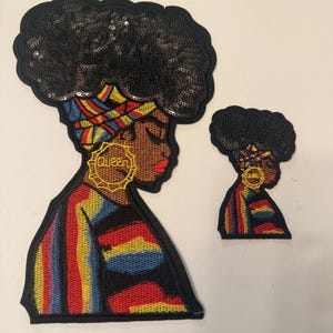 May include: Two embroidered patches featuring a profile of a woman with a sequined afro. The larger patch has a colorful striped top and gold earrings that read "Queen". The smaller patch mirrors the design.