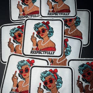 May include: Embroidered patches featuring a retro-style woman with blue hair, red sunglasses, and a red dress, giving the middle finger. The word "RESPECTFULLY" is embroidered below the image. Patches are square with a white border.