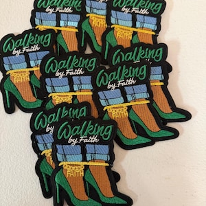 May include: A collection of embroidered patches featuring a pair of green high-heeled shoes, blue cuffed jeans, and a gold chain anklet with the word FAITH. The text Walking by Faith is embroidered in green script above the shoes.