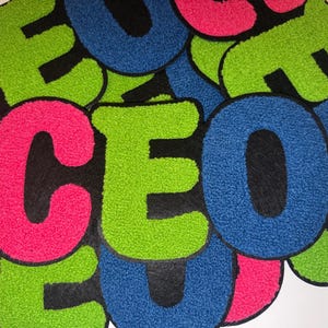 Peut inclure: Un ensemble d'&eacute;cussons color&eacute;s et textur&eacute;s &eacute;pelant "CEO". Les lettres sont en rose vif, vert et bleu, avec un support noir. Ces &eacute;cussons sont probablement destin&eacute;s aux v&ecirc;tements ou aux accessoires.