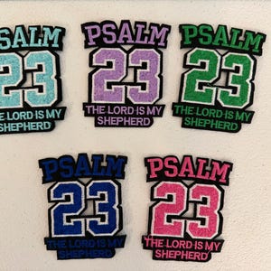 May include: Five embroidered patches featuring the text PSALM 23 and THE LORD IS MY SHEPHERD. Each patch has a large number 23 in the center with a black border. The colors include light blue, light purple, green, dark blue, and bright pink.